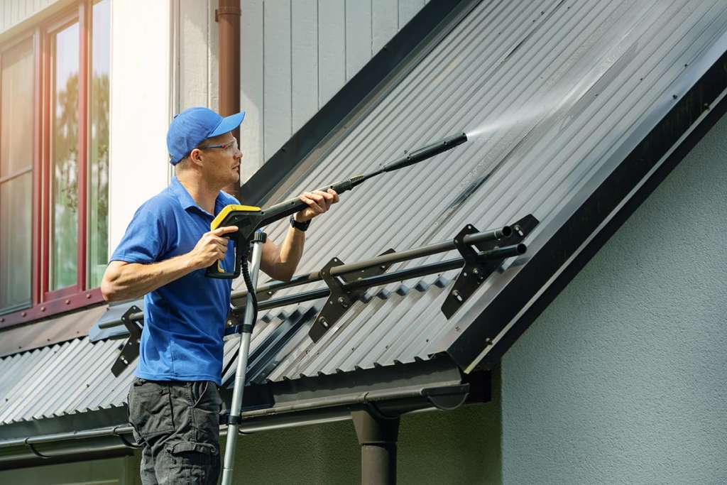Man power washing roof of home
