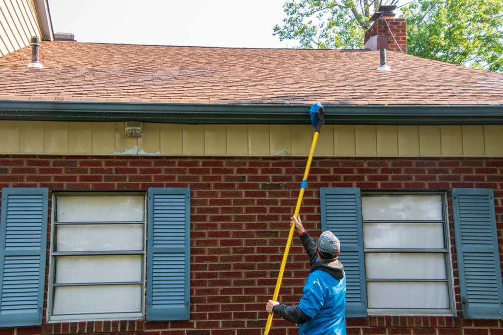Man cleaning gutter on red brick house